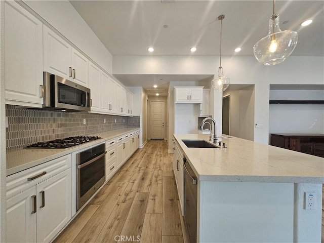 kitchen featuring appliances with stainless steel finishes, white cabinetry, decorative light fixtures, and sink