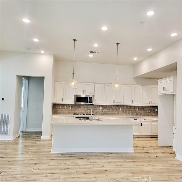 kitchen with stainless steel appliances, white cabinetry, pendant lighting, and an island with sink