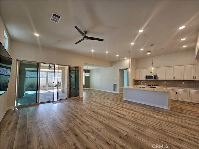 kitchen featuring a center island with sink, white cabinetry, ceiling fan, and hanging light fixtures