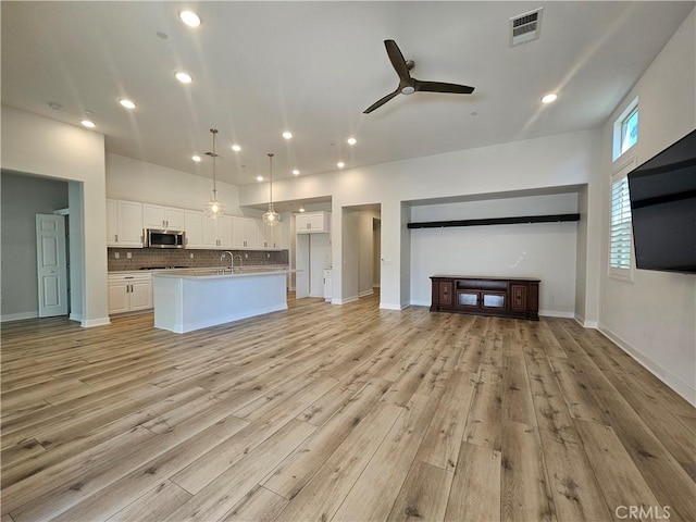 unfurnished living room with sink, ceiling fan, and light wood-type flooring