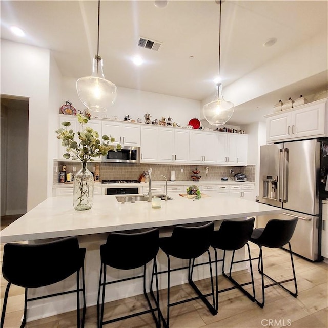 kitchen featuring a large island with sink, decorative light fixtures, sink, and appliances with stainless steel finishes