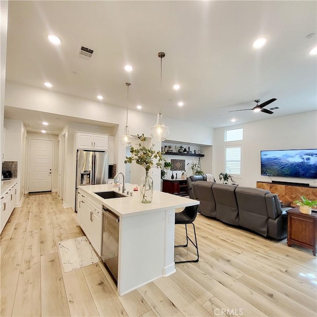 kitchen with a kitchen island with sink, appliances with stainless steel finishes, ceiling fan, sink, and decorative light fixtures