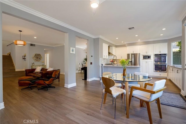 dining room with sink, hardwood / wood-style floors, and ornamental molding