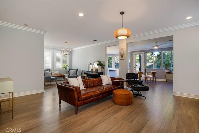 living room with hardwood / wood-style floors, ceiling fan with notable chandelier, ornamental molding, and a healthy amount of sunlight