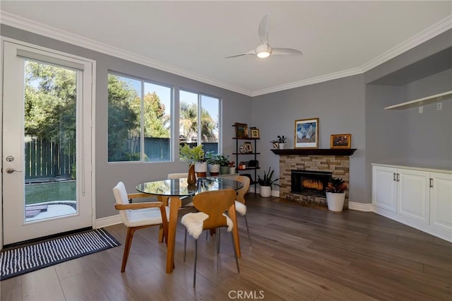 dining area with a stone fireplace, crown molding, ceiling fan, and dark wood-type flooring