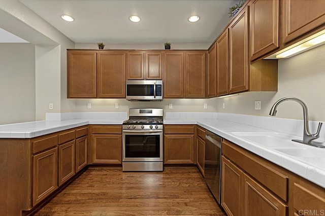 kitchen featuring tile counters, sink, stainless steel appliances, dark hardwood / wood-style flooring, and kitchen peninsula