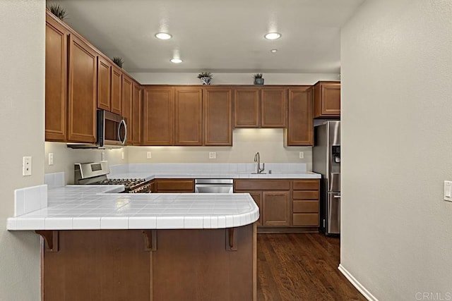 kitchen featuring tile countertops, a breakfast bar, dark wood-type flooring, kitchen peninsula, and stainless steel appliances