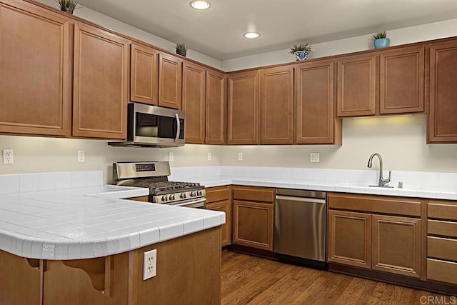 kitchen featuring sink, tile counters, dark hardwood / wood-style floors, kitchen peninsula, and appliances with stainless steel finishes