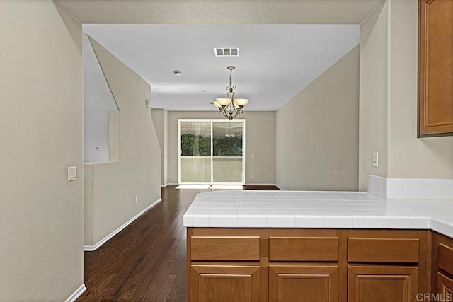 kitchen featuring tile counters, an inviting chandelier, dark hardwood / wood-style floors, kitchen peninsula, and pendant lighting