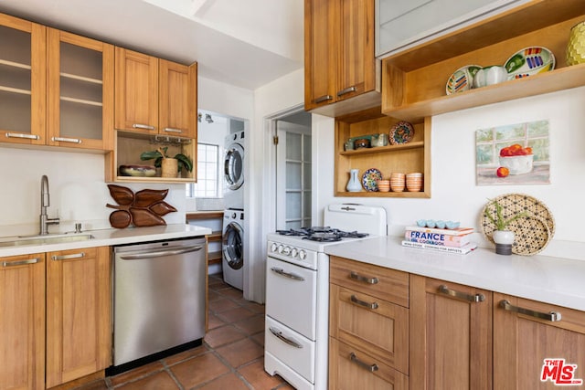 kitchen with stainless steel dishwasher, white gas stove, dark tile patterned floors, sink, and stacked washer / drying machine