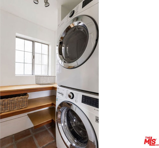 laundry area with dark tile patterned floors and stacked washer / drying machine