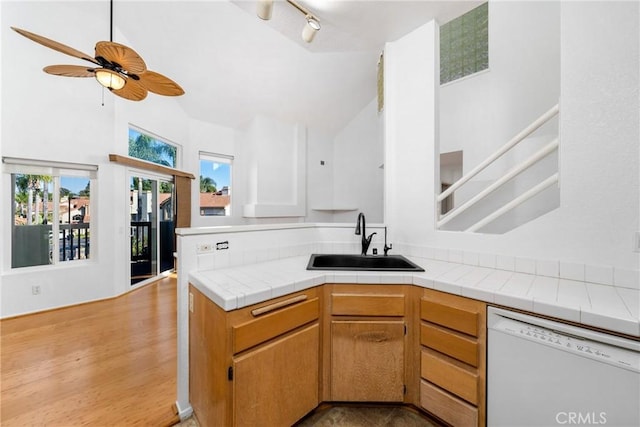 kitchen featuring dishwasher, sink, light hardwood / wood-style flooring, ceiling fan, and tile counters