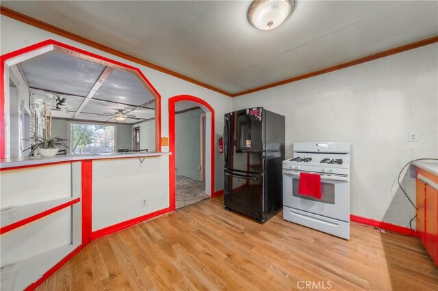 kitchen featuring gas range gas stove, ceiling fan, crown molding, black refrigerator, and light wood-type flooring