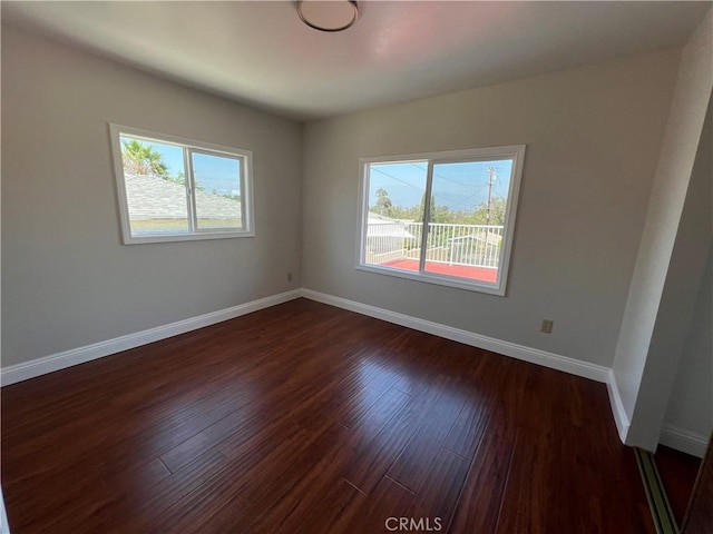 empty room with a wealth of natural light and dark hardwood / wood-style floors