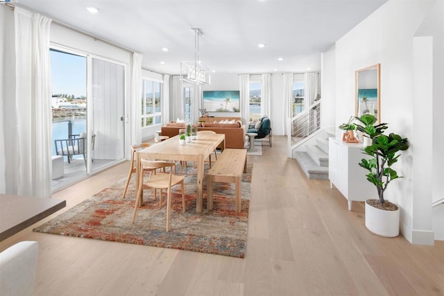 dining area featuring a water view, light wood-type flooring, a wealth of natural light, and an inviting chandelier