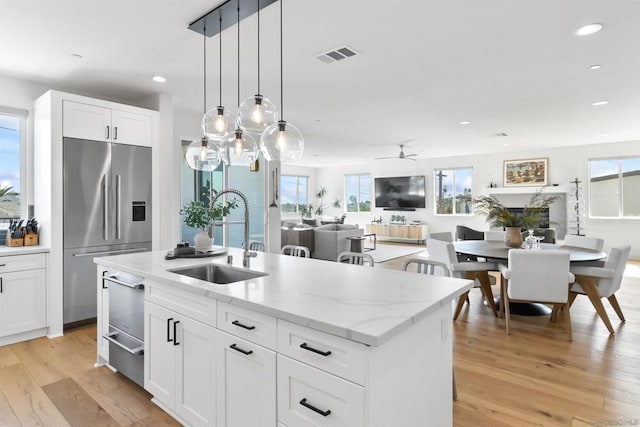 kitchen featuring sink, stainless steel built in fridge, white cabinetry, ceiling fan, and an island with sink