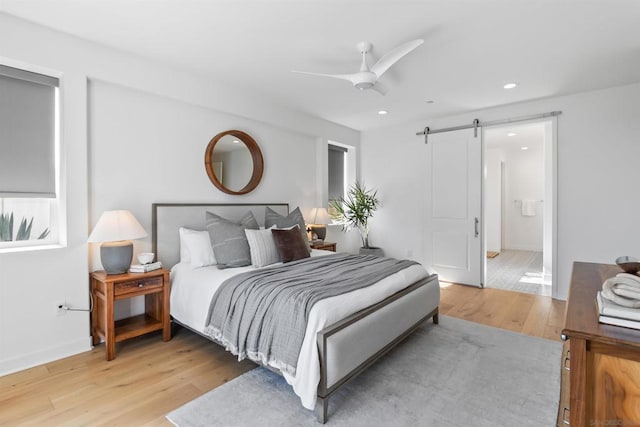 bedroom featuring hardwood / wood-style flooring, ceiling fan, and a barn door