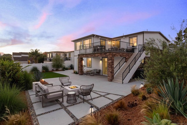 back house at dusk featuring a fire pit, a patio area, and a balcony