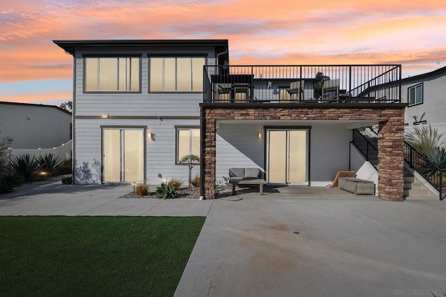 back house at dusk featuring a balcony and a patio area