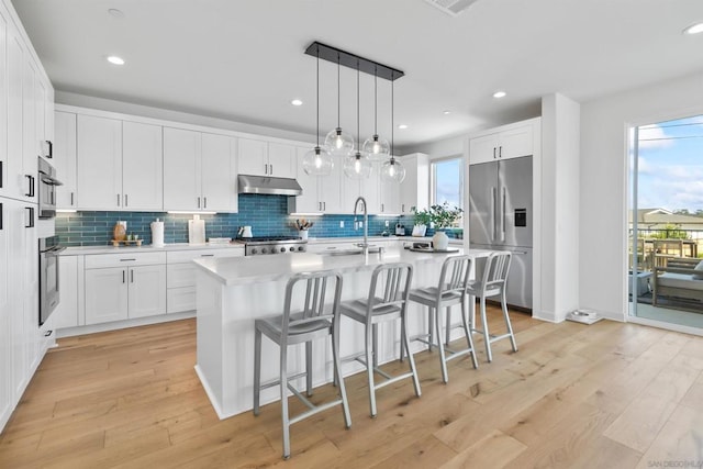 kitchen featuring white cabinetry, stainless steel built in fridge, sink, and a kitchen island with sink