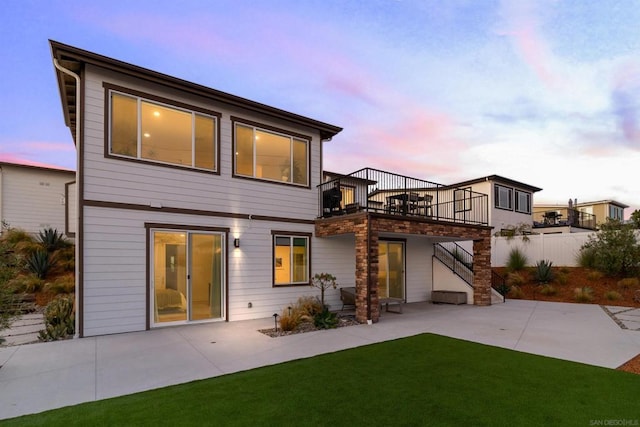 back house at dusk with a yard, a patio area, and a balcony