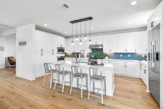 kitchen featuring sink, white cabinetry, stainless steel appliances, a center island with sink, and light wood-type flooring