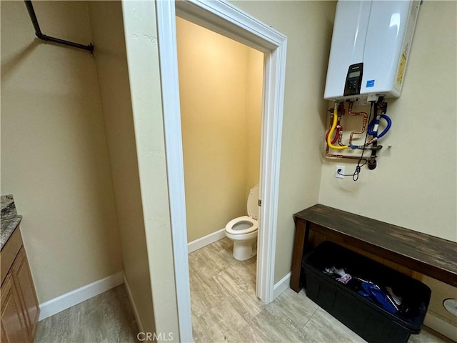 bathroom featuring hardwood / wood-style floors, vanity, tankless water heater, and toilet