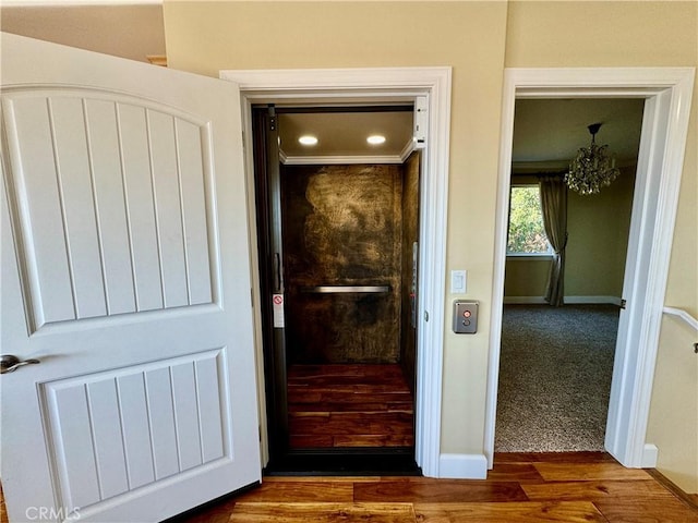 hall with elevator, dark hardwood / wood-style floors, crown molding, and a notable chandelier