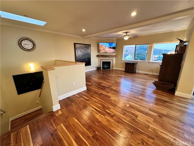 unfurnished living room featuring hardwood / wood-style flooring, a skylight, crown molding, and ceiling fan