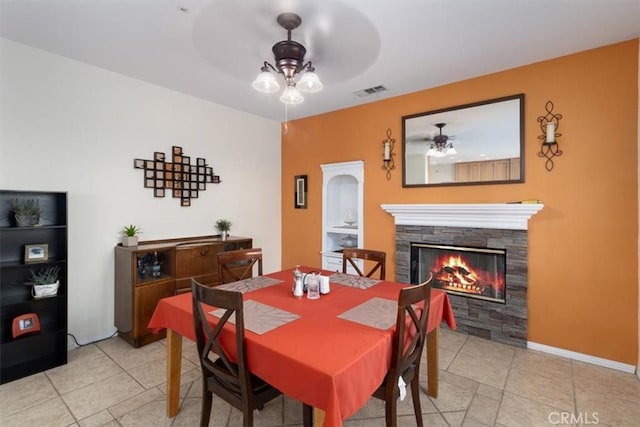 dining space featuring ceiling fan, a stone fireplace, and light tile patterned floors