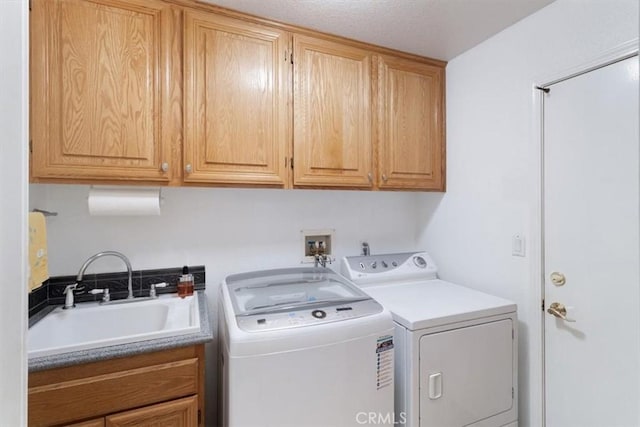 clothes washing area with washing machine and clothes dryer, a textured ceiling, cabinets, and sink