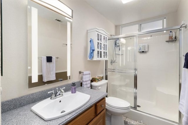 bathroom featuring vanity, a shower with shower door, and toilet