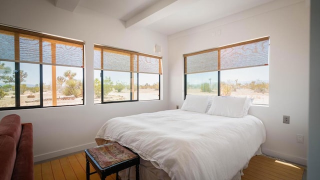 bedroom featuring beam ceiling, multiple windows, and hardwood / wood-style floors