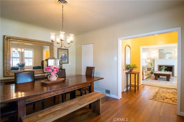 dining room featuring hardwood / wood-style floors, an inviting chandelier, and a brick fireplace