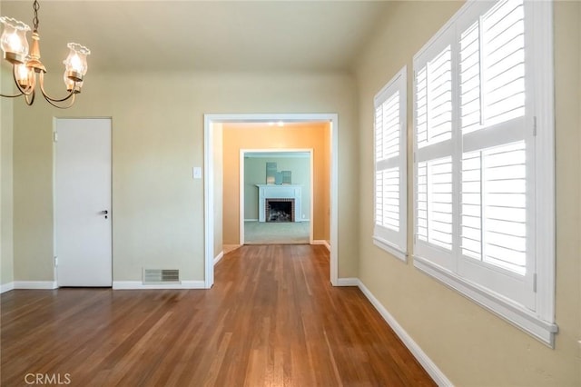 hallway with visible vents, baseboards, an inviting chandelier, and wood finished floors