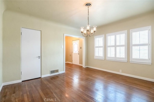 unfurnished dining area featuring visible vents, baseboards, an inviting chandelier, and wood finished floors