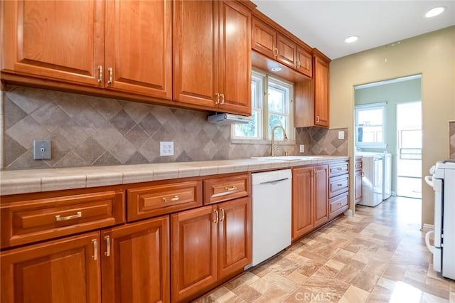 kitchen with washing machine and clothes dryer, tasteful backsplash, brown cabinets, white appliances, and a sink