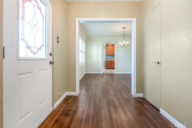 foyer entrance with dark wood-type flooring, a notable chandelier, and baseboards