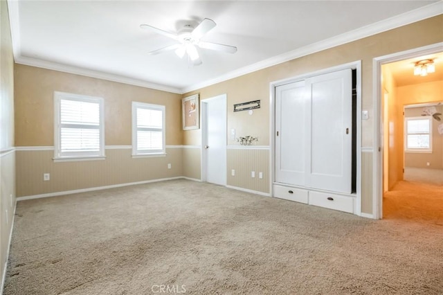 unfurnished bedroom featuring a ceiling fan, a closet, carpet, wainscoting, and crown molding