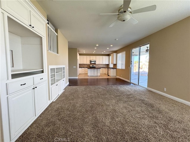 unfurnished living room featuring ceiling fan and dark carpet