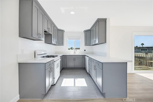 kitchen featuring kitchen peninsula, white appliances, gray cabinets, and sink