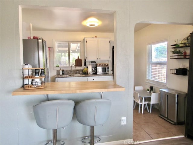 kitchen featuring butcher block counters, sink, stainless steel appliances, a kitchen bar, and white cabinets