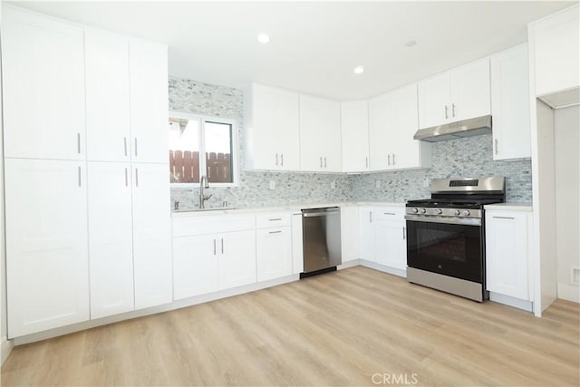 kitchen featuring appliances with stainless steel finishes, tasteful backsplash, white cabinetry, sink, and light wood-type flooring