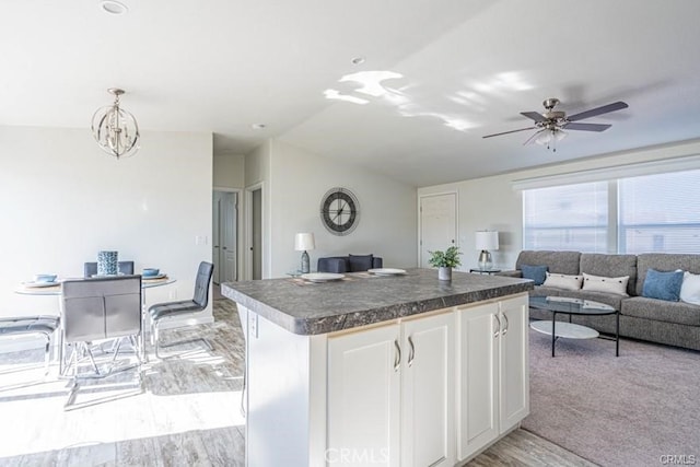 kitchen featuring white cabinets, ceiling fan with notable chandelier, light colored carpet, and hanging light fixtures