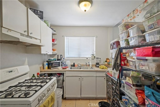 kitchen featuring light tile patterned flooring, white cabinetry, white gas range, and sink