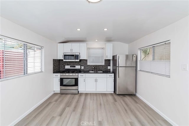 kitchen with backsplash, sink, light hardwood / wood-style floors, white cabinetry, and stainless steel appliances