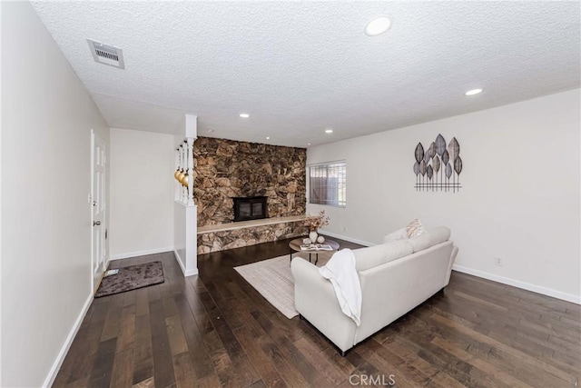 living room featuring a textured ceiling, dark hardwood / wood-style flooring, and a stone fireplace