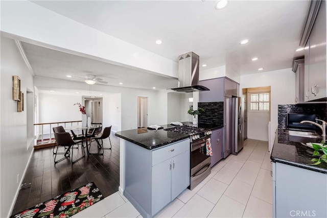 kitchen with appliances with stainless steel finishes, island range hood, ceiling fan, sink, and light hardwood / wood-style floors