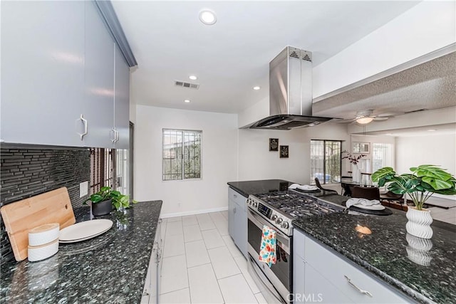 kitchen featuring ceiling fan, stainless steel range with gas cooktop, island exhaust hood, dark stone counters, and light tile patterned floors