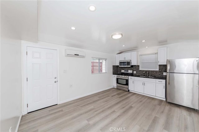 kitchen with a wall mounted AC, white cabinets, light hardwood / wood-style flooring, appliances with stainless steel finishes, and tasteful backsplash